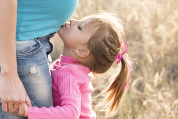 妊婦の母親のお腹にキスをする幼い娘