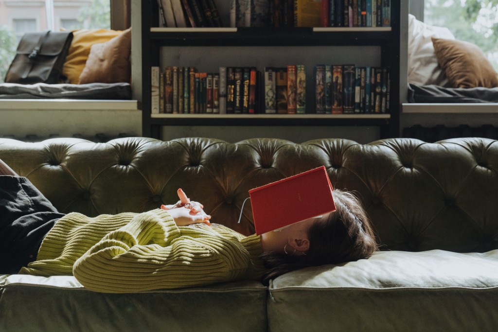 顔に本を置きソファーに横たわる女性