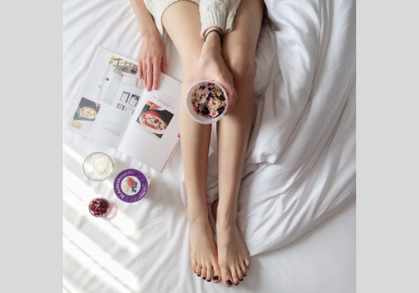 ダイエットのためのヘルシーフードと本を読むベッドの上にいる女性の足